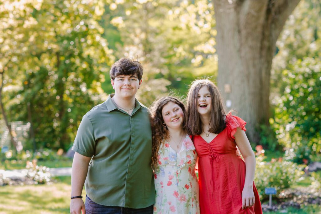 Three siblings smile the camera during their family photography session with Christy Rice Photography at Columbus Park of Roses in Columbus, Ohio.