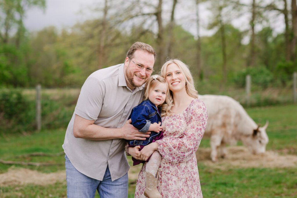 Parents hold their one year old daughter while smiling at the camera during their family photography session with Christy Rice Photography at Cooper's Knoll Farm in Pataskala, Ohio.