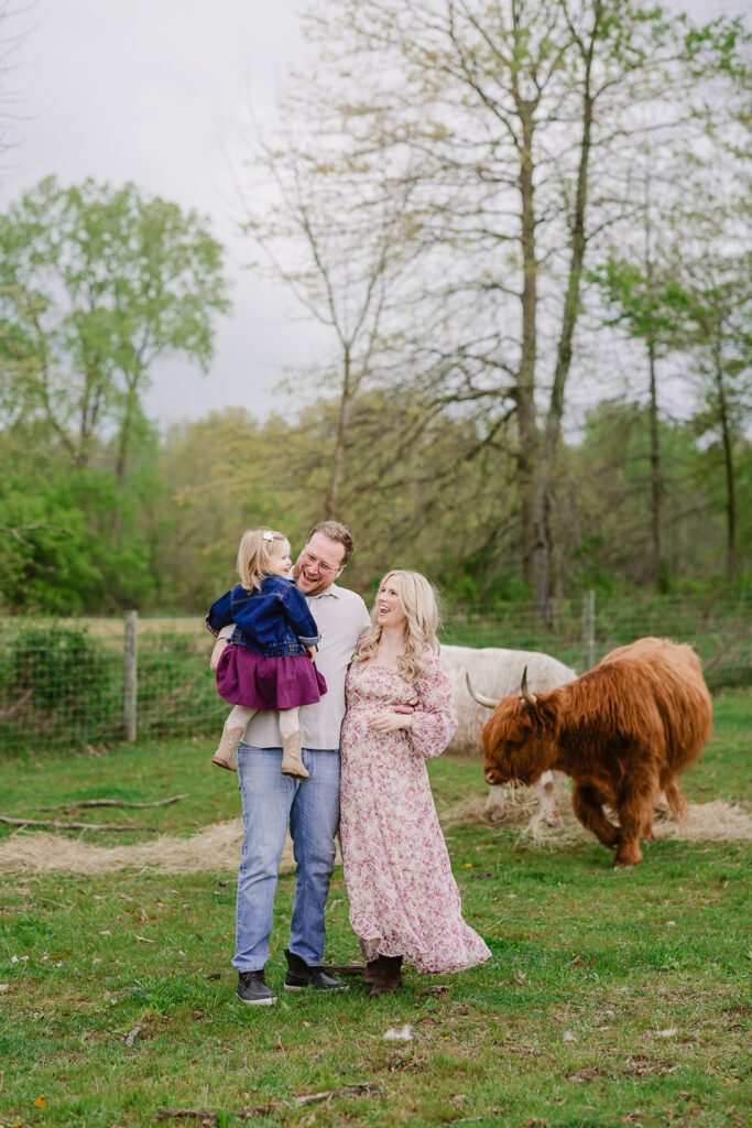 Parents hold their one year old daughter while smiling at the camera during their family photography session with Christy Rice Photography at Cooper's Knoll Farm in Pataskala, Ohio.