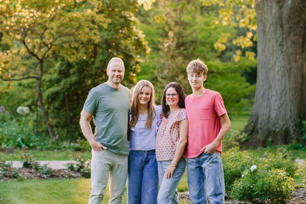 A family of four smiles at the camera during their family photography session with Christy Rice Photography at Columbus Park of Roses in Columbus, Ohio.