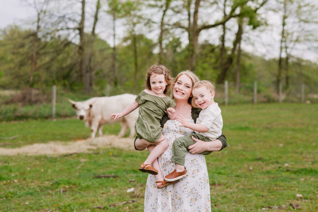 A mom holds her smiling two year old twins, during their family photography session with Christy Rice Photography at Cooper's Knoll Farm in Pataskala, Ohio