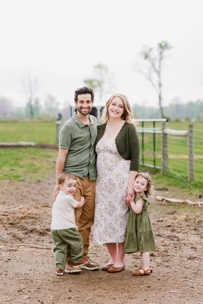 A family of four, a mom and dad and two year old twins, pose in a farm field during their family photography session with Christy Rice Photography at Cooper's Knoll Farm in Pataskala, Ohio